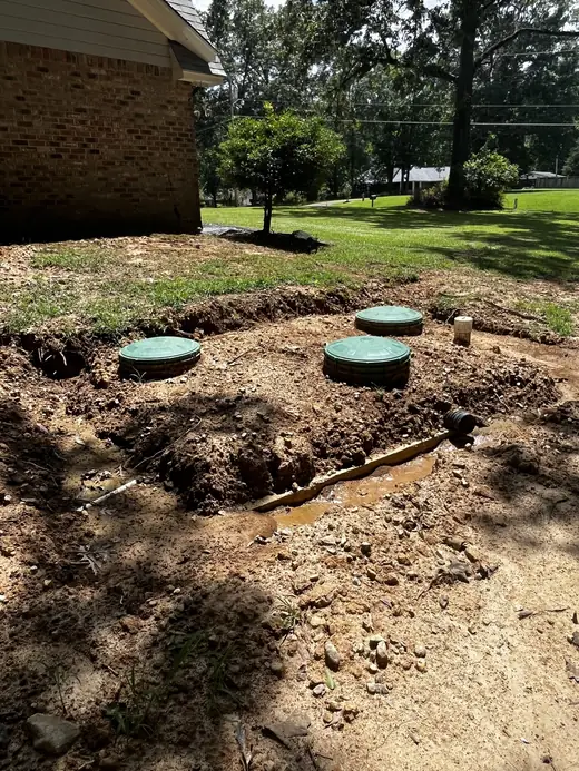 A finished Seal Digging septic installation beside a brick house, three green riser lids set flush into fresh clay