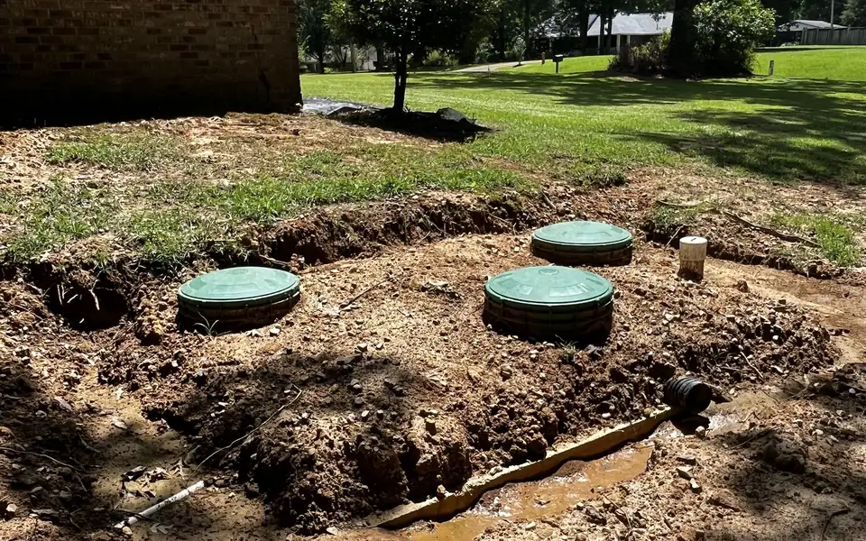 A finished Seal Digging septic installation beside a brick house in Florence, Mississippi, with three green riser lids set flush into fresh clay